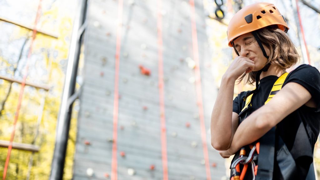 A woman wearing indoor rock climbing gear closes her eyes in distress