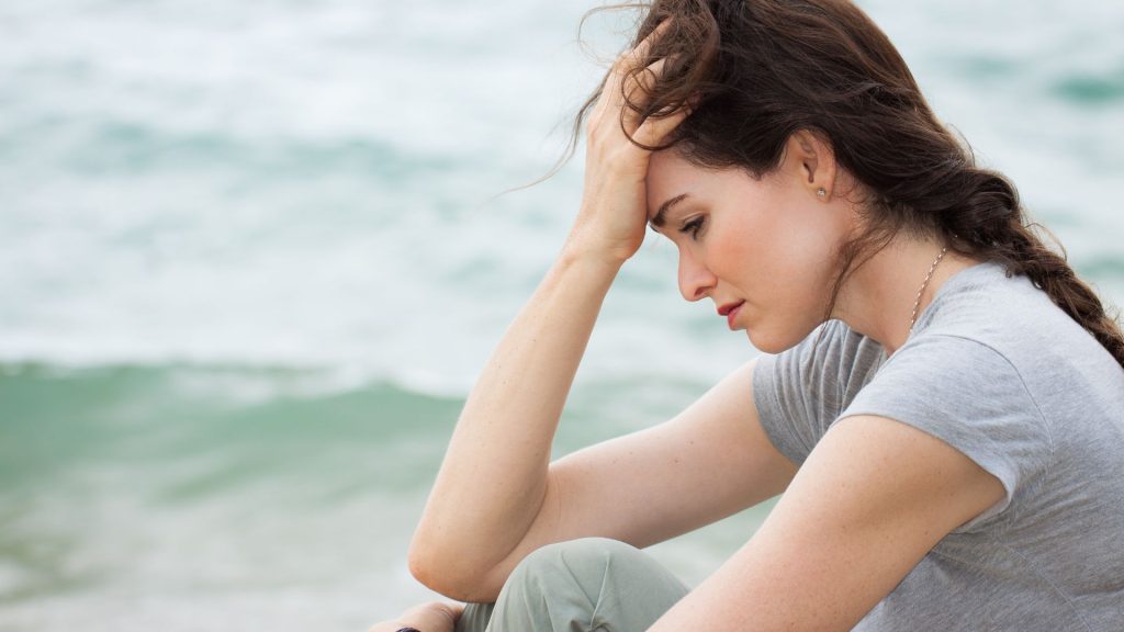 A grief-stricken looking woman sitting near the ocean