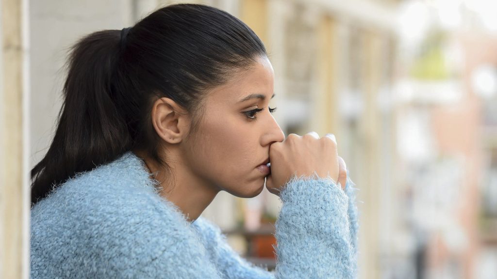 A close up image of a depressed looking woman looking out through an apartment window