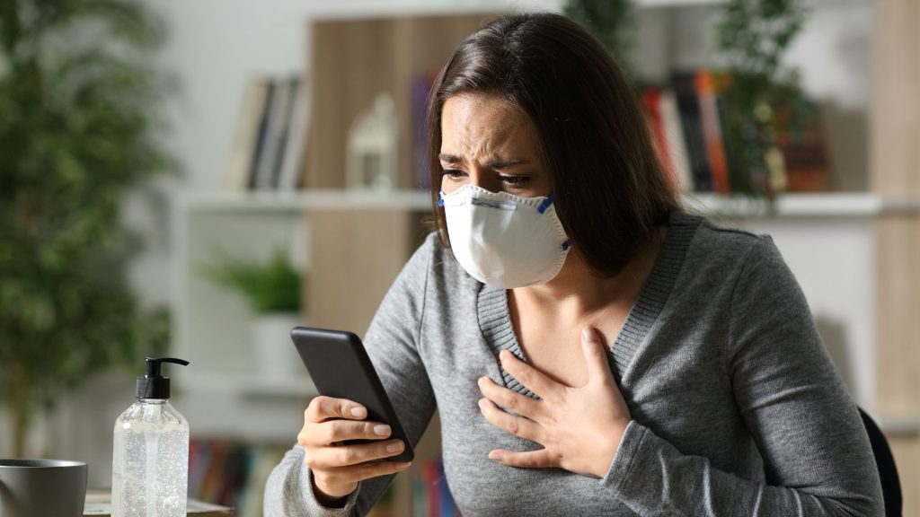 A woman with an N95 mask and hand sanitizer nearby talks on the phone