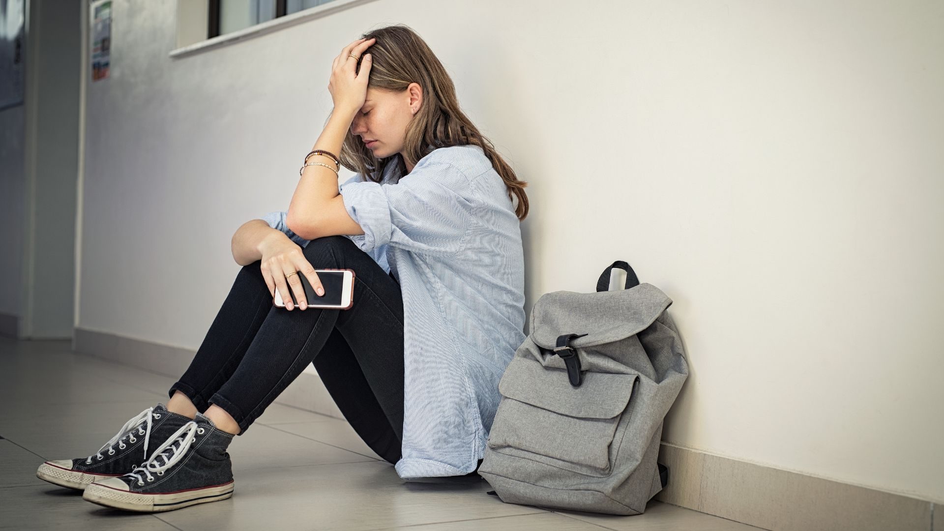 A distressed school age girl sits on a floor