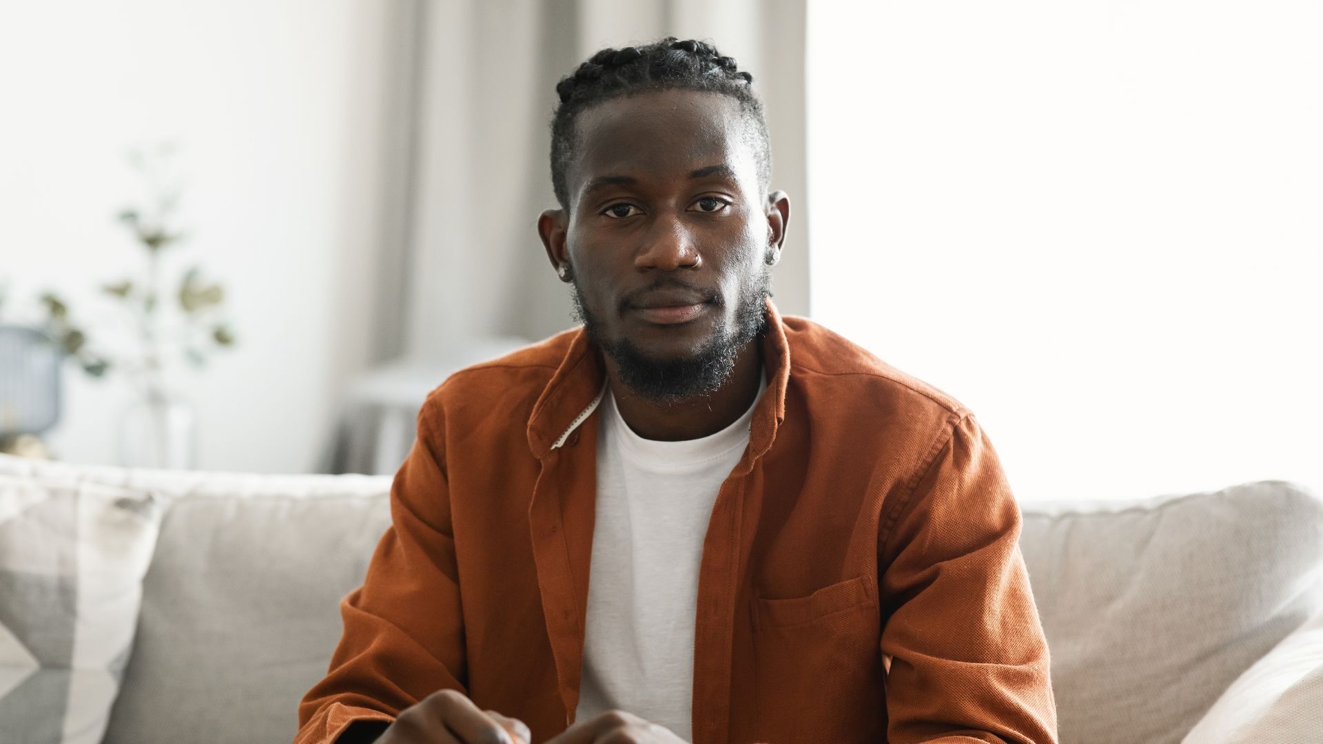 A man on a couch looks toward a camera with a calm expression