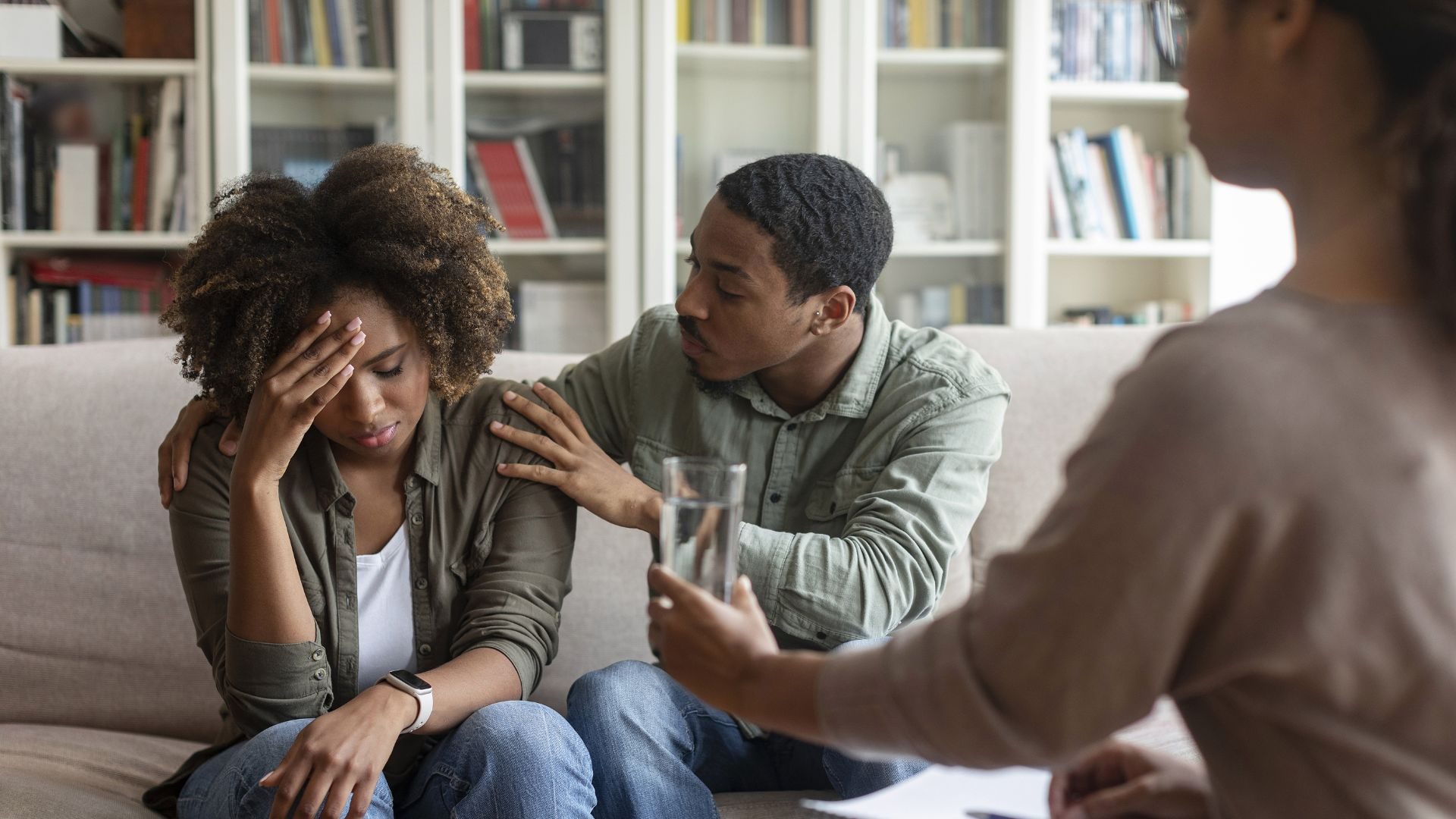 A man comforts his girlfriend while a therapist hands her water