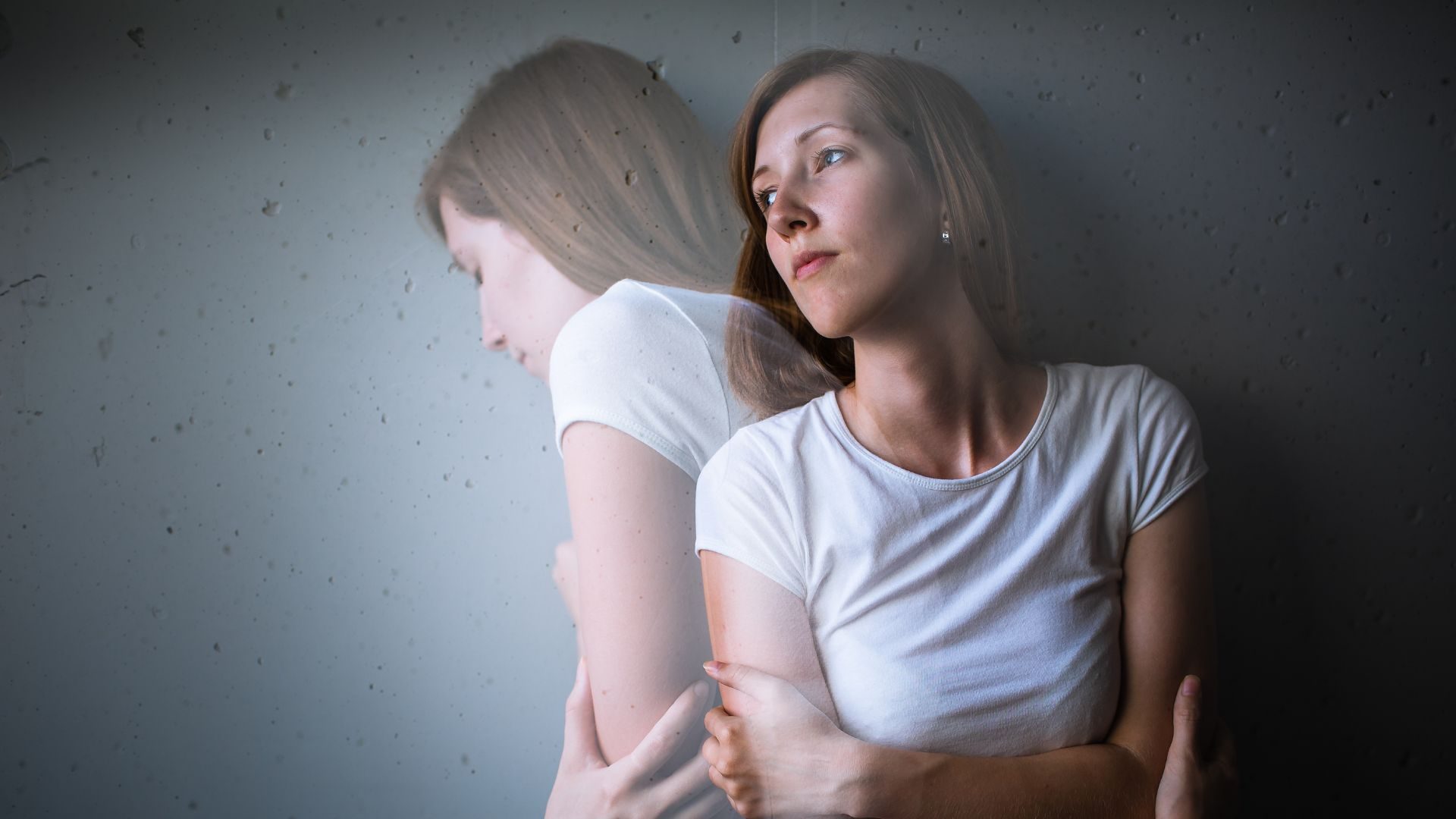 An edited photograph of a woman looking calm, but a semi-opaque version of herself in distress