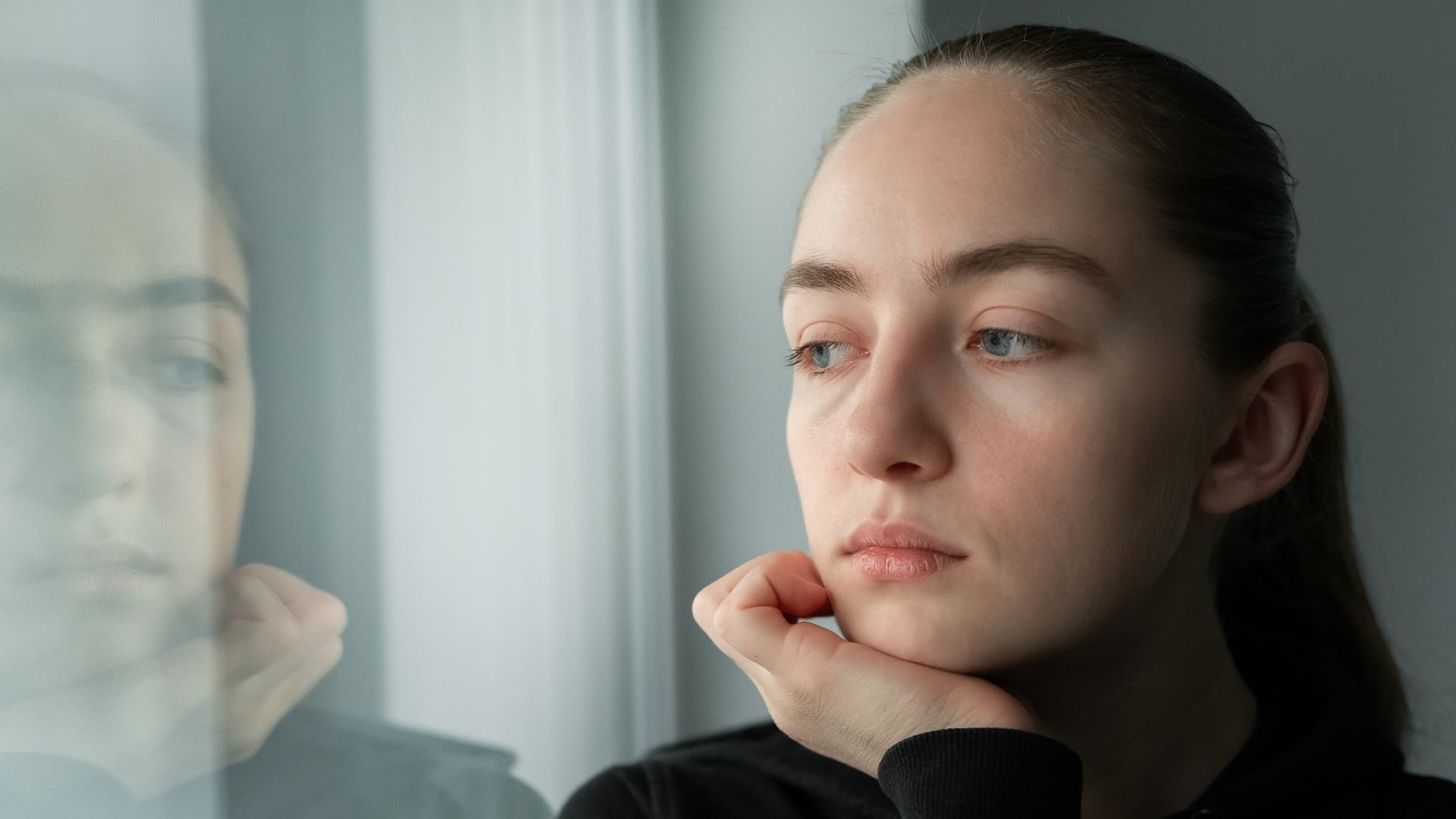A melancholy looking woman looks out through a window