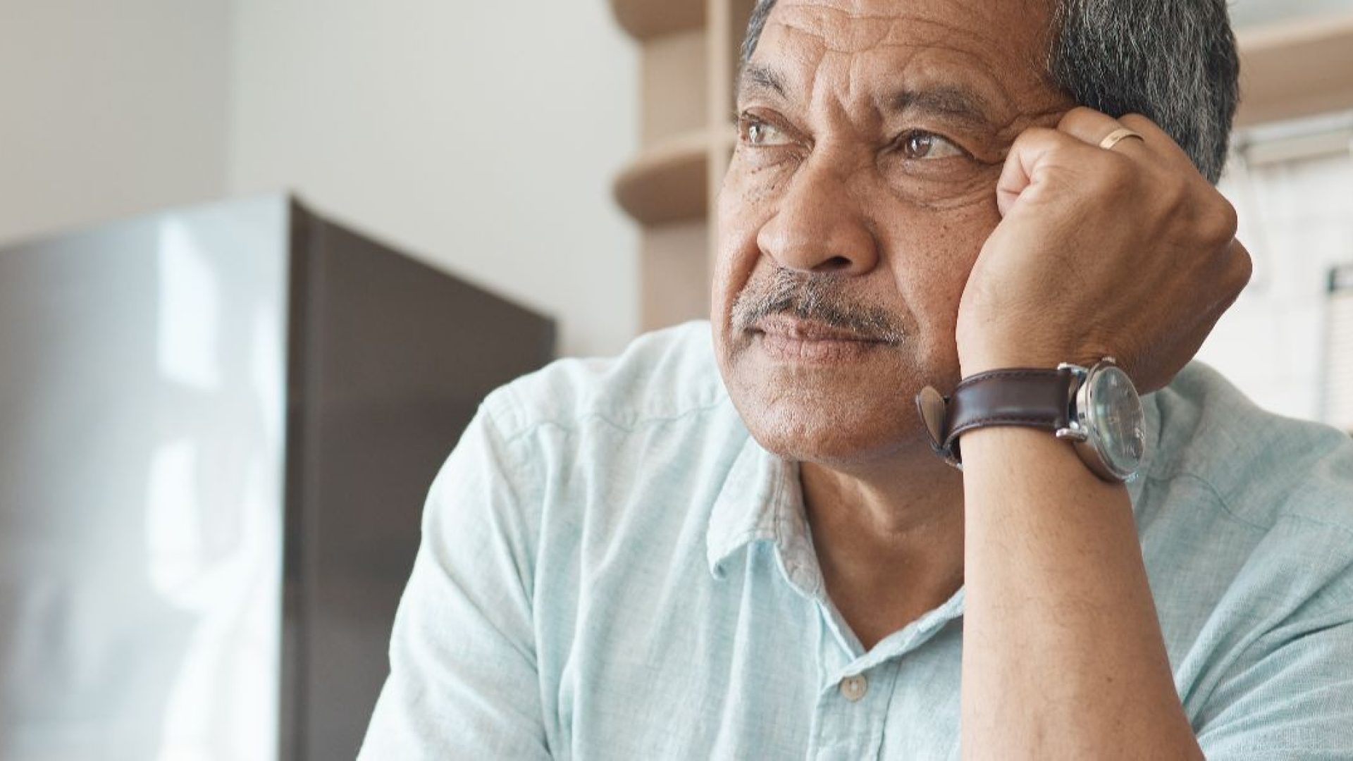Someone sits in a kitchen, looking worried.