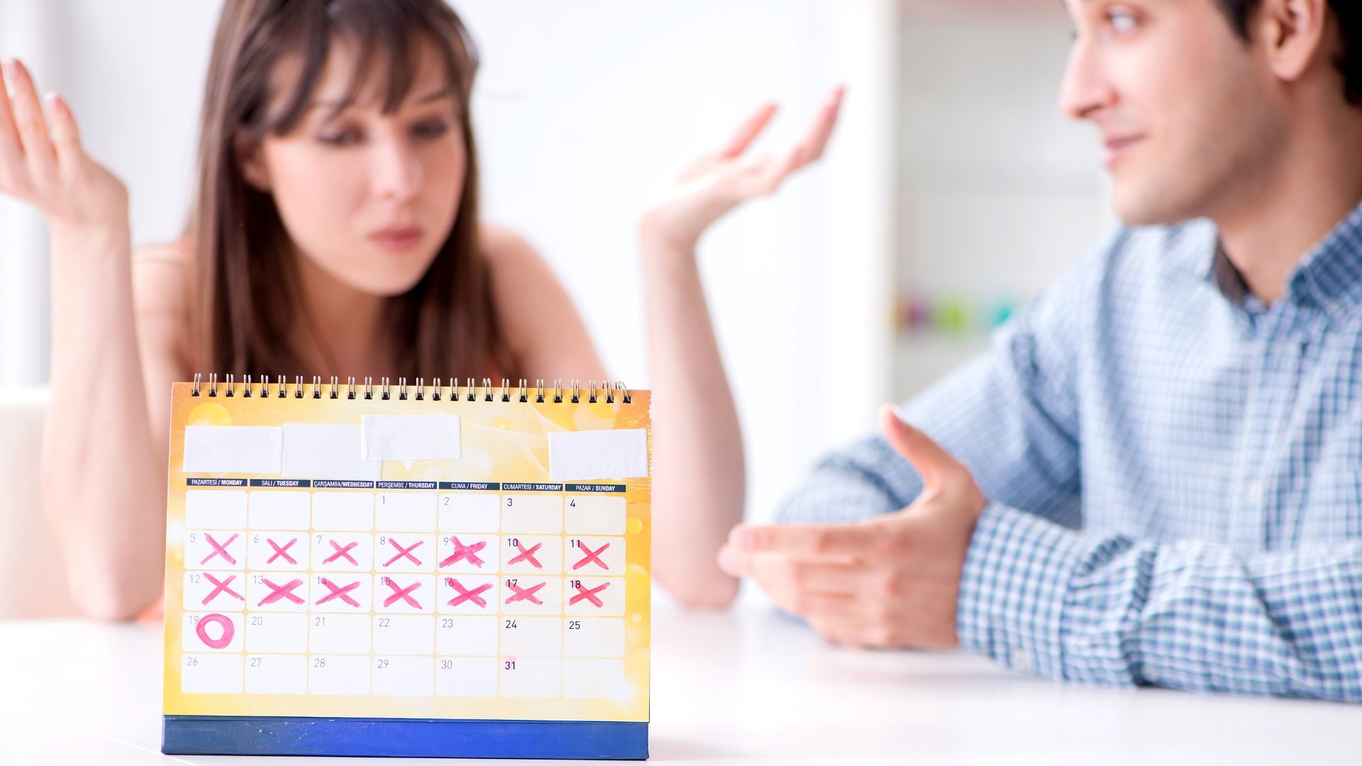 A calendar with lots of Xs and one O, and behind it, a couple having a discussion at a table