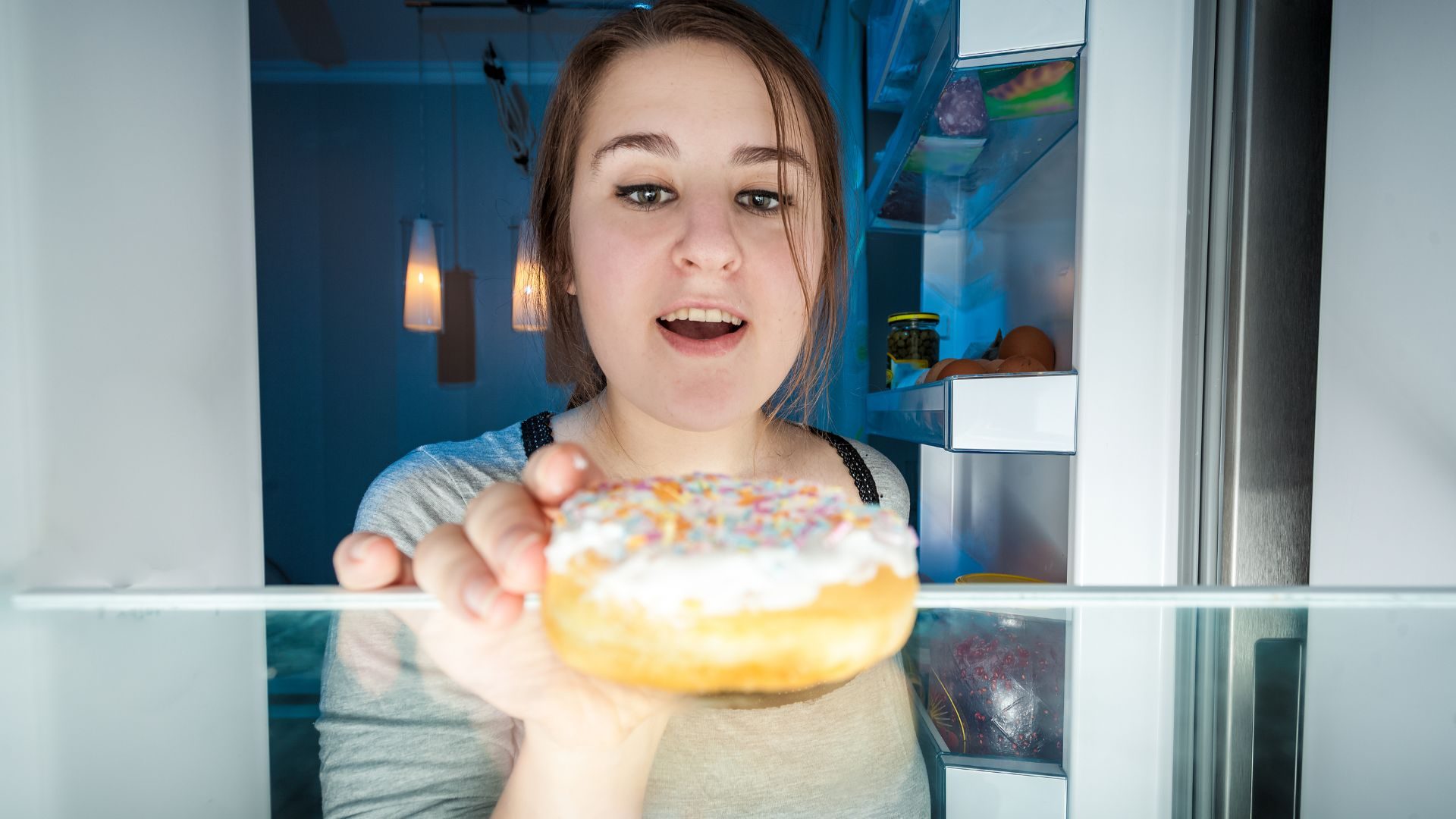 A woman reaches into a refrigerator for a donut