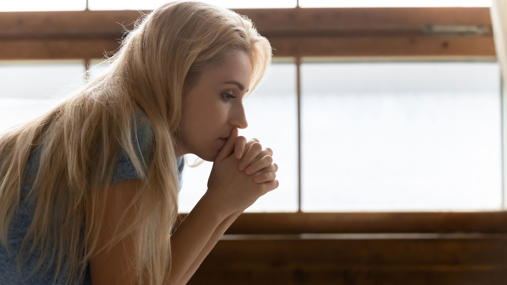 A distressed woman with her hands to her face looks off into the distance