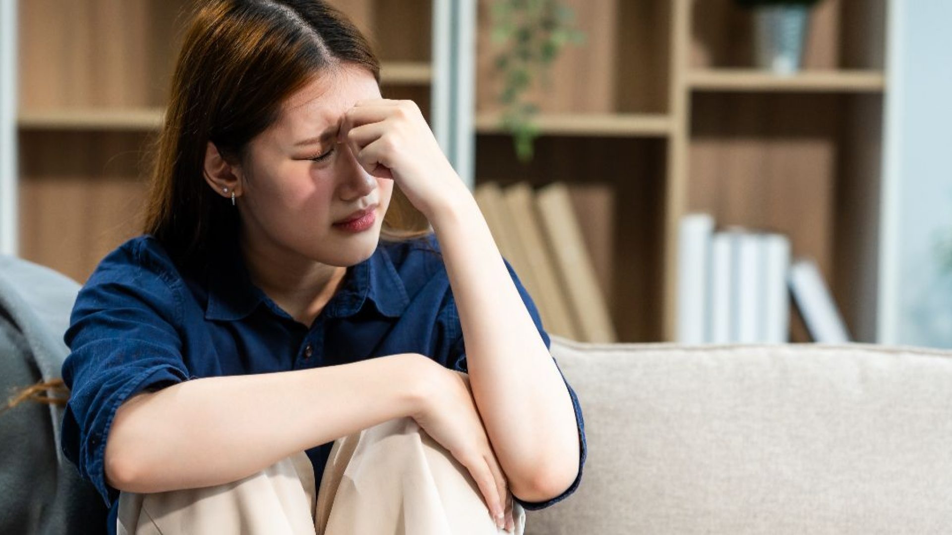 Someone sits on the couch with their knees to the chest, feeling overwhelmed.