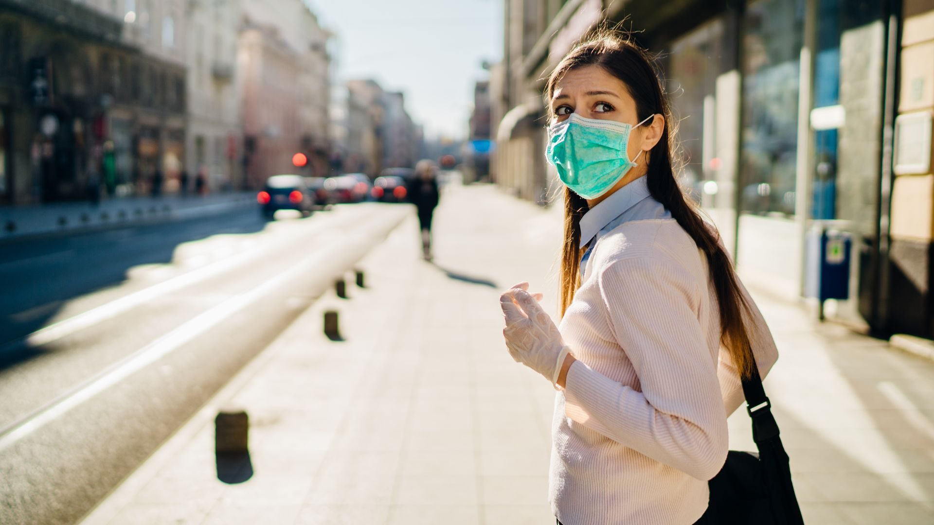 A woman with a mask and rubber gloves in public looks over her shoulder