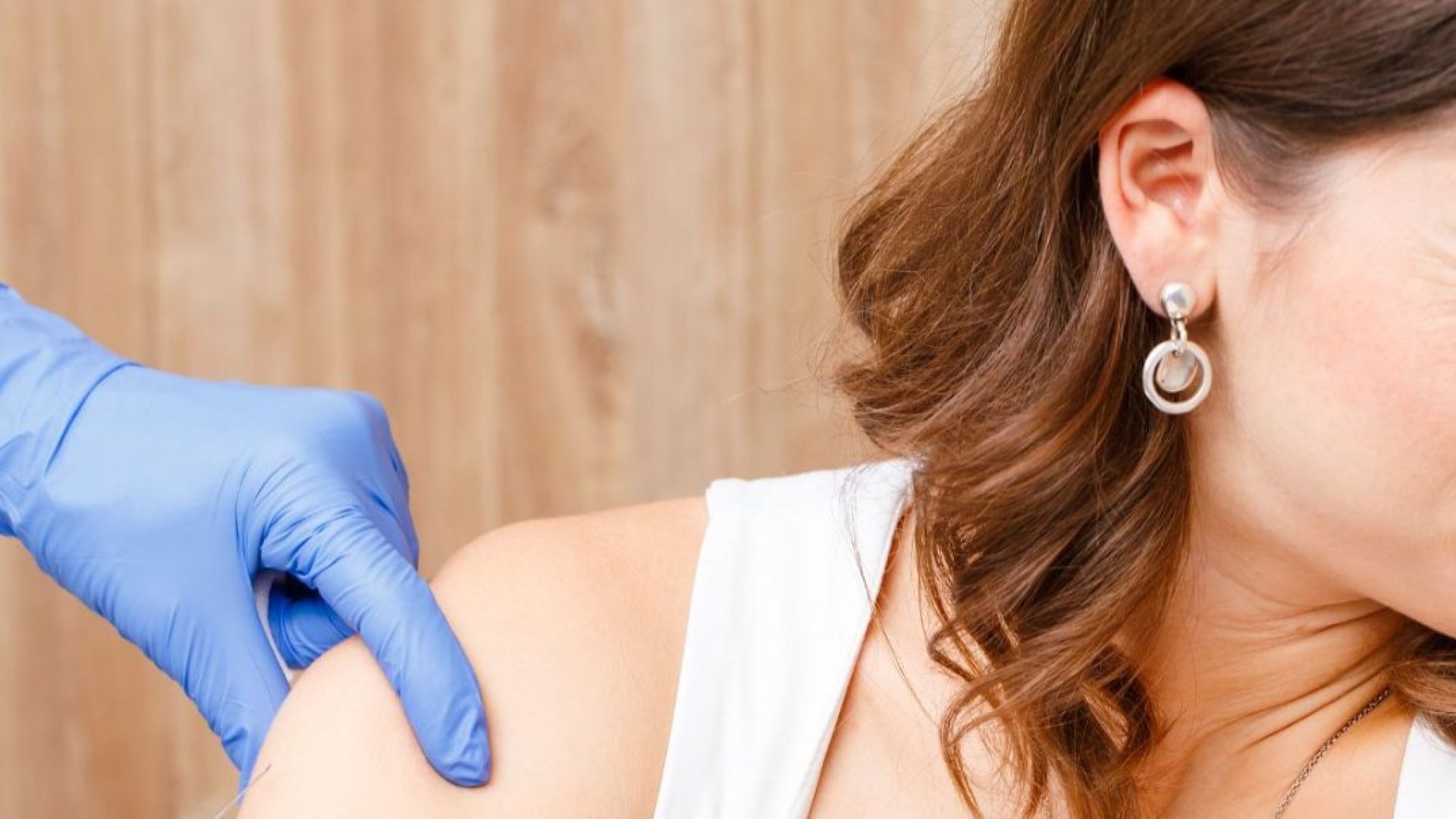 Someone with their face screwed up in fear and looking away, a gloved nurse's hand on their arm, implying they are getting a shot out of frame.