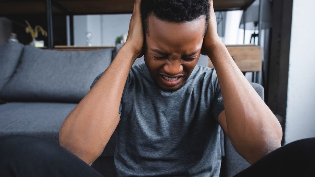 A young man grits his teeth, closes his eyes, and puts his hands up to the side of his head