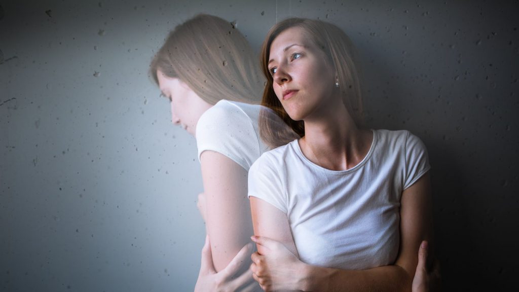 An edited photograph of a woman looking calm, but a semi-opaque version of herself in distress