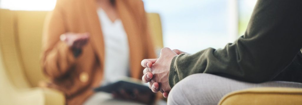 A therapist talks to a patient, only hands and bodies visible.