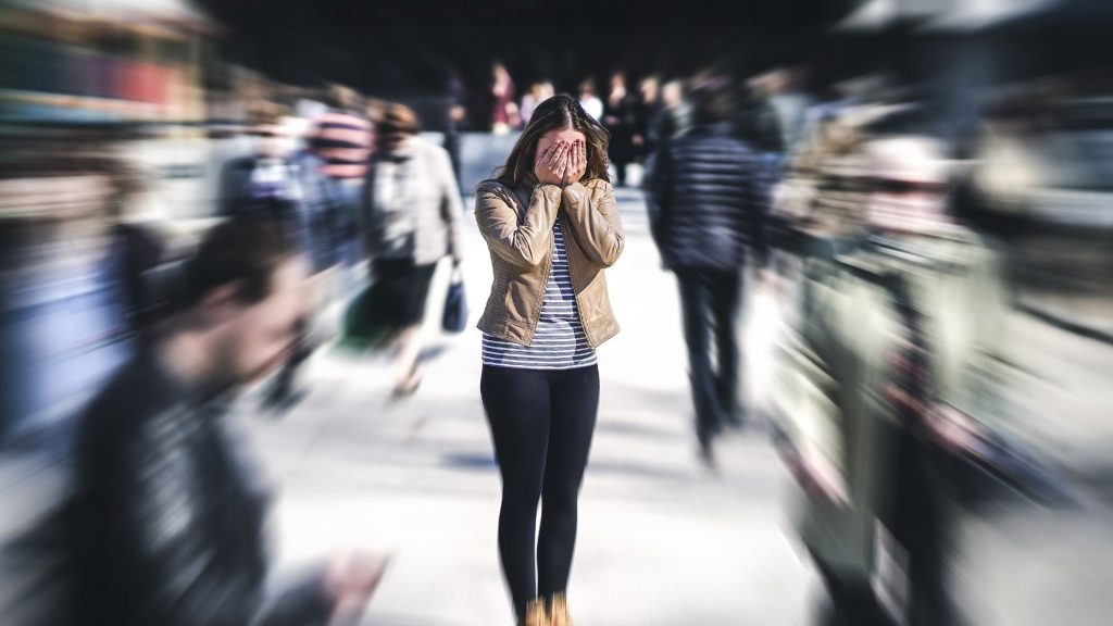 A distressed woman covering her face while a crowd of people around her are edited into a blur