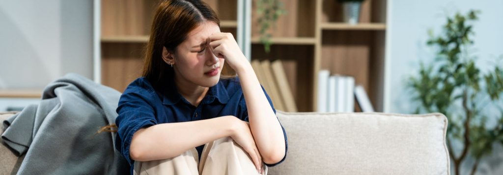 Someone sits on the couch with their knees to the chest, feeling overwhelmed.