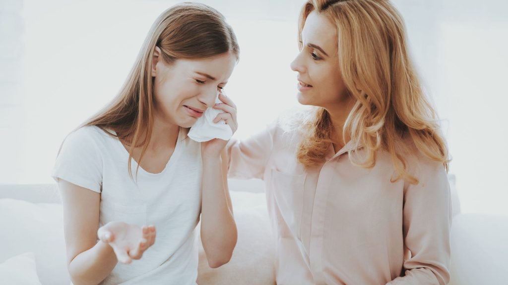 A crying teenager is comforted by a middle aged woman