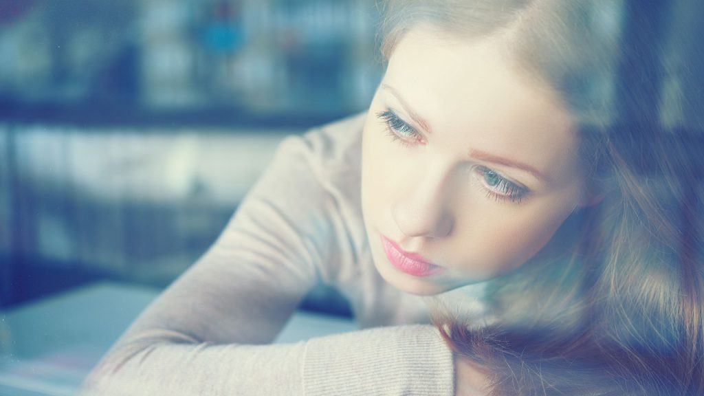 A distressed woman looks out through a window