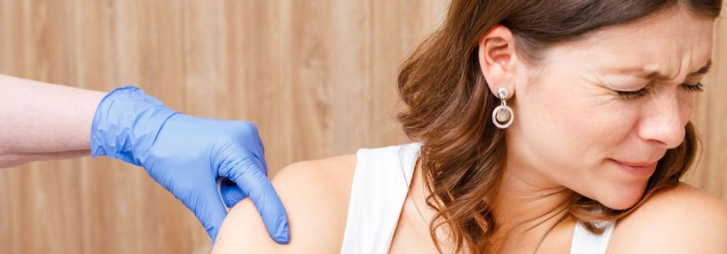 Someone with their face screwed up in fear and looking away, a gloved nurse's hand on their arm, implying they are getting a shot out of frame.